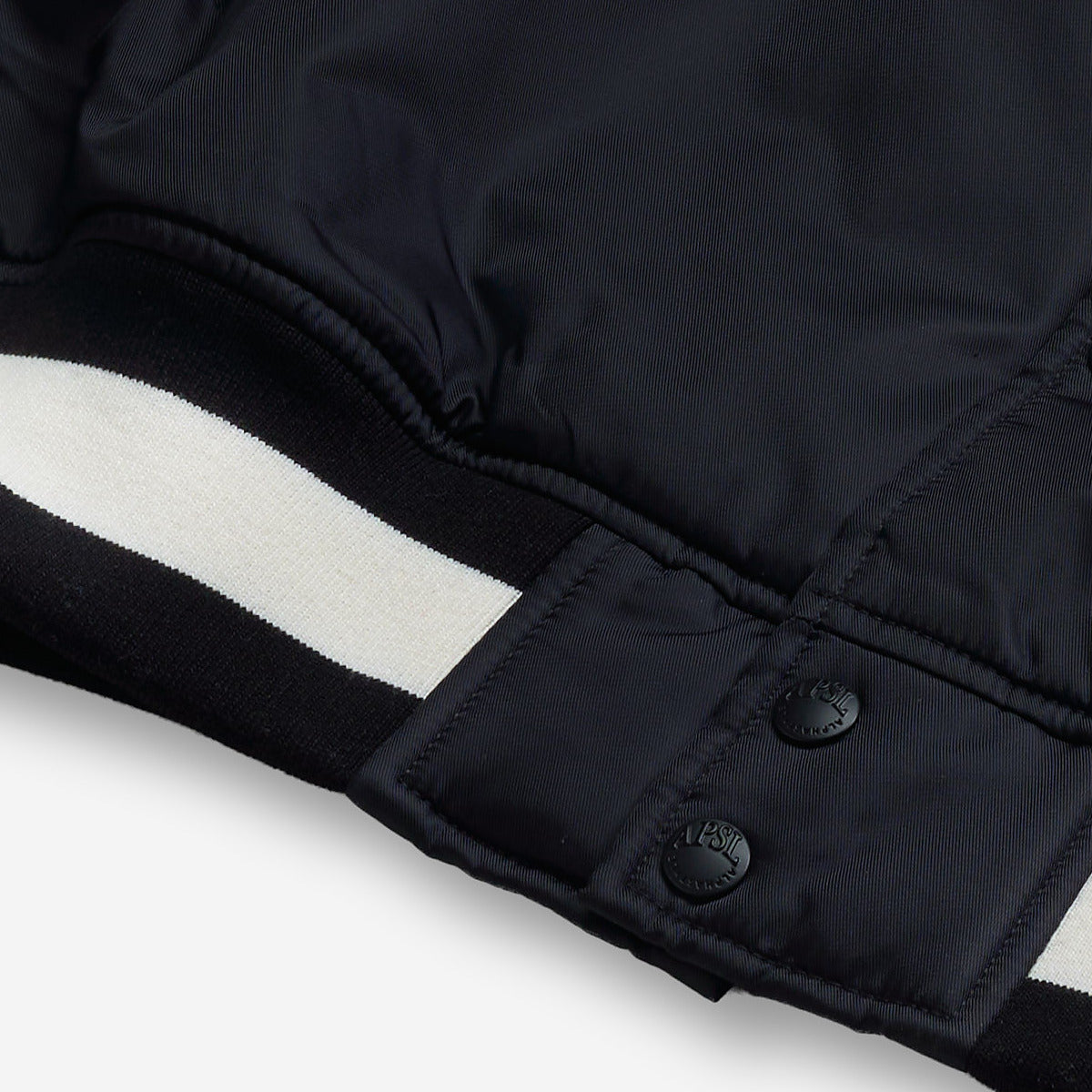 AlphaStyle Barren Varsity Jacket in Black – Detailaufnahme von Saumbund und Druckknopfleiste mit schwarz-weißem Rippstrick