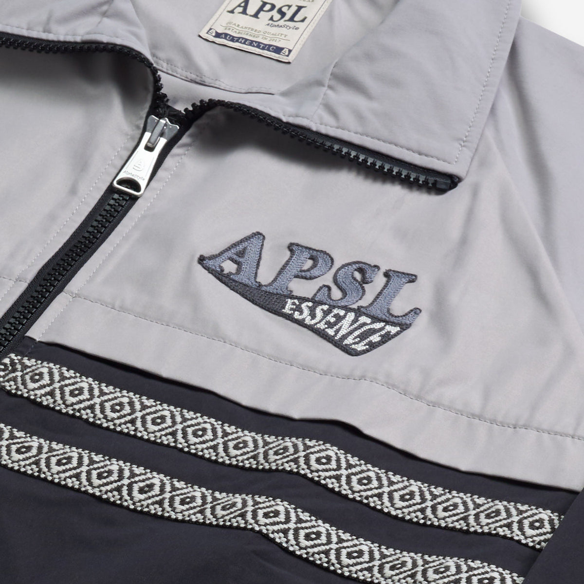 AlphaStyle Whitman Batwing Windbreaker Jacket in Black/Grey – Detailaufnahme der APSL-Essence-Stickerei neben dem Frontreißverschluss