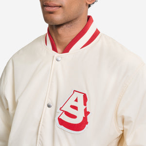 AlphaStyle Barren Varsity Jacket in Bone – Nahaufnahme des roten AS-Chenille-Patches auf cremeweißem Nylon