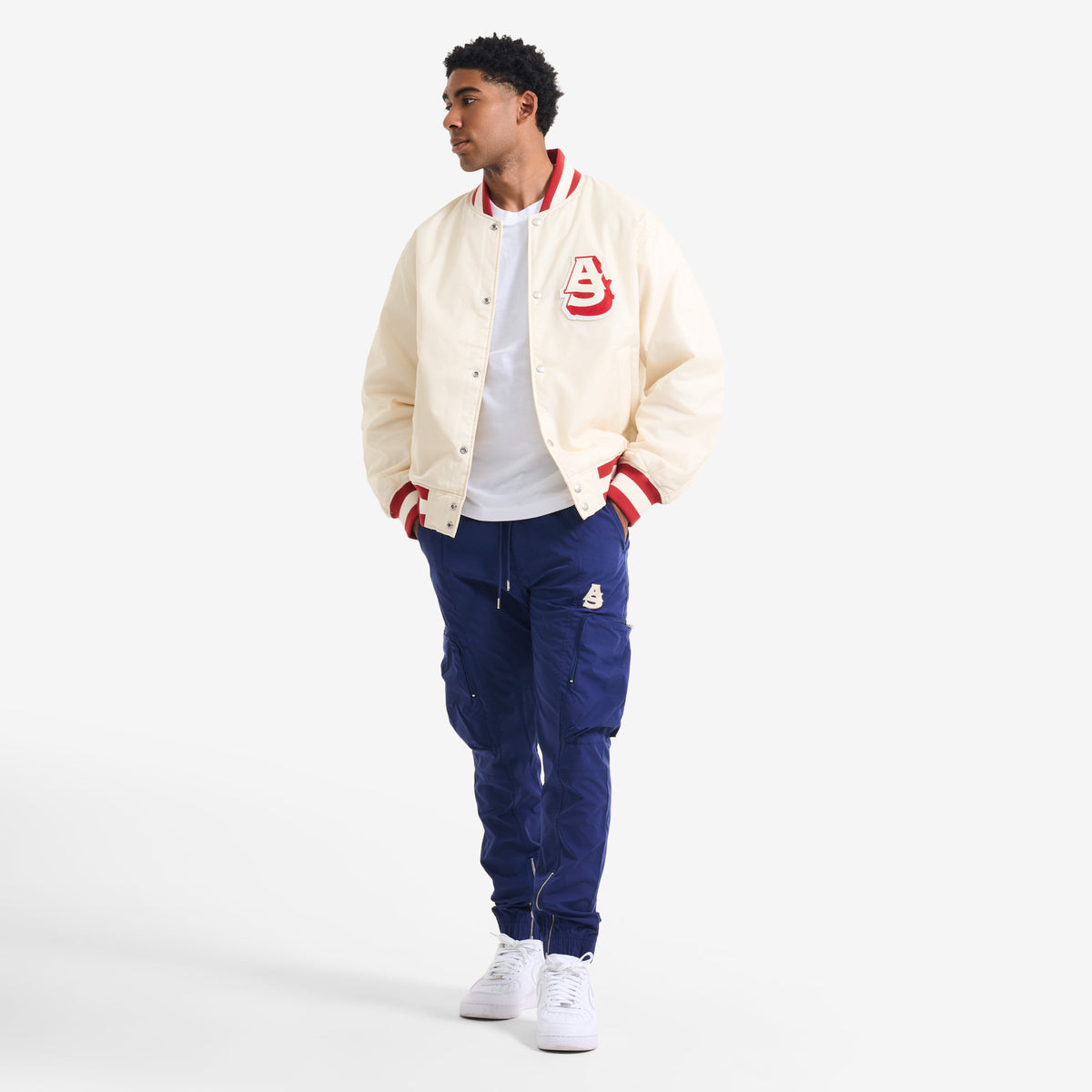 AlphaStyle Barren Varsity Jacket in Bone – Seitliche Ganzkörperaufnahme am Model, kombiniert mit blauer Cargohose