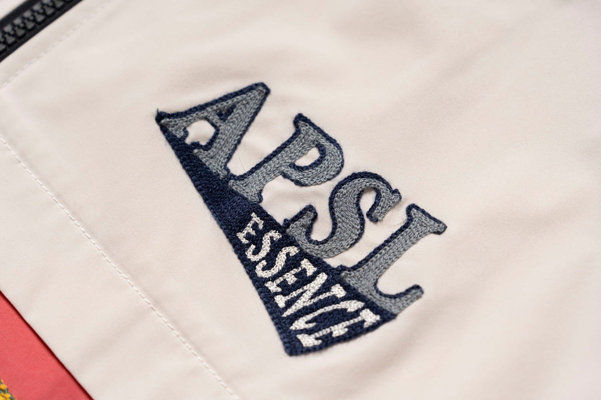 AlphaStyle Whitman Batwing Windbreaker Jacket – Detailansicht der gestickten APSL-Essence-Applikation in Navy auf Bone